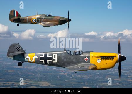 Dieses Bild zeigt einen Hawker Sea Hurrikan Mk10 der Royal Air Force, Kennzeichen G-CHTK, Seriennummer P2921, Militärcode GZ-L, der in Formation mit deutschen Luftwaffenflugzeugen einschließlich eines Hispano HA-1112-M1L Buchon fliegt, der einen Messerschmitt Bf-109 repräsentiert, Kennzeichen G-AWHH, Code 9, Seriennummer 145. Das Foto zeigt Piloten aus nächster Nähe während der Luft-Luft-Manöver bei den UK Warbirds 2025 und zeigt britische und deutsche Kampfflugzeuge aus dem Zweiten Weltkrieg. Der Sea Hurricane verfügt über einen Rolls-Royce Merlin-Motor und ein einziehbares Fahrwerk. Stockfoto