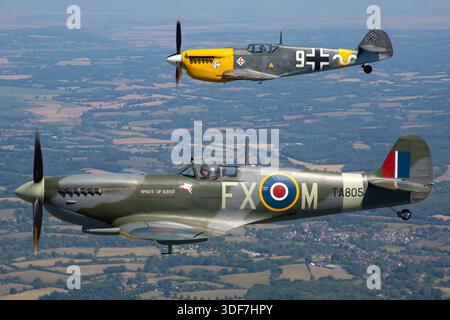 Abgebildet ist ein Royal Air Force Supermarine 361 Spitfire HF9E, Seafire-Variante, Kennzeichen G-PMNF, Seriennummer TA805, Code FX-M, benannt nach Spirit of Kent. Daneben fliegt eine deutsche Luftwaffe Hispano HA-1112-M1L Buchon, die einen Messerschmitt Bf-109, Kennzeichen G-AWHH, Code 9, Seriennummer 145 darstellt. Das Foto betont die Nahaufnahmen der Piloten während der Formation und der Luft-Luft-Manöver bei den UK Warbirds 2025 und veranschaulicht den Einsatz von Kampfflugzeugen aus dem Zweiten Weltkrieg. Stockfoto