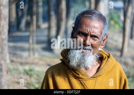 Kishoreganj, Bangladesch - 18. Dezember 2025 - Nahaufnahme eines ranghohen Mannes aus Bangladesch mit langem grauen Bart in einem gelben Hoodie. Dorflehrer s Stockfoto