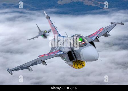 Air-to-Air-Bild, das zwei tschechische Luftwaffe Saab JAS 39C Gripen zeigt, die während der NATO-Tage 2025 in engem Formationszustand flogen. Die Flugzeuge sind 9234 und 9240 registriert, mit den Seriennummern 39234 und 39240, und sind in einem Gedenkschema zur Feier des 20-jährigen Gripen-Dienstes gemalt. Das Foto bietet Nahaufnahmen der Piloten in ihren Cockpits. Zu den wichtigsten Merkmalen gehören Delta-Flügel, Kanarenvorflugzeuge und einzelne General Electric F414G Turbofan-Motoren, die NATO-Operationen unterstützen. Stockfoto