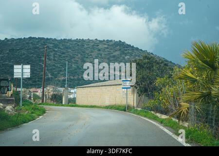 Ein Straßenschild, das den Eingang zum Dorf Melidoni auf Kreta markiert. Umgeben von üppiger grüner Vegetation, Zitrusbäumen und einer traditionellen Steinmauer Stockfoto