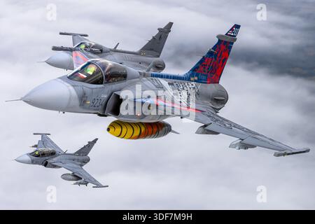 Luft-Luft-Foto, das die tschechischen Luftwaffe Saab JAS 39C und JAS 39D Gripen zeigt, die an den NATO-Tagen 2025 teilnahmen. Das Bild zeigt einsitzige JAS 39C-Jäger, die 9234 und 9240 registriert sind, und eine zweisitzige JAS 39D, registriert 9819. Die Flugzeuge tragen eine Gedenklackierung zur Feier des 20-jährigen Dienstes. Nahaufnahmen der Cockpits zeigen Piloten im Flug. Der Gripen ist ein Mehrzweckjäger mit Delta-Flügeln, Canards und einem Volvo RM12 Turbofan-Motor. Stockfoto