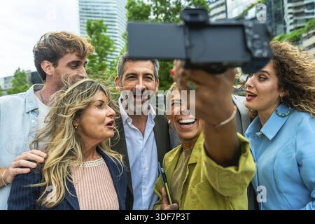 Eine Gruppe verschiedener Geschäftsleute und Kollegen genießt einen Moment zusammen, lacht und lächelt, während sie draußen ein Selfie macht Stockfoto