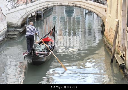 Ein Gondolierer fährt seine Gondelbahn unter einer Brücke auf einem ruhigen Kanal, Venedig, Veneto, Italien Stockfoto