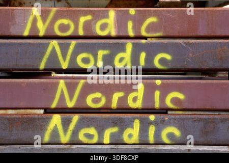 Rostfreie Stahlträger, die auf einem Schrottplatz aufeinander gestapelt sind, auf jedem der Schilder ist das Wort Nordic in Gelb lackiert Stockfoto
