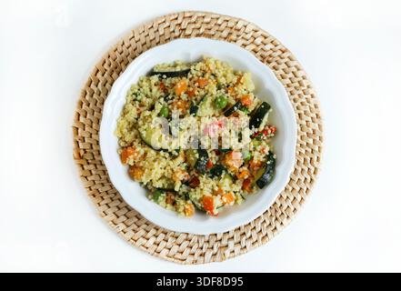 Couscous mit gekochtem Gemüse wie Karotten, Zucchini, Paprika, Erbsen und frischer Petersilie auf weißem Hintergrund. Gesundes, veganes und vegetarisches Essen. Stockfoto