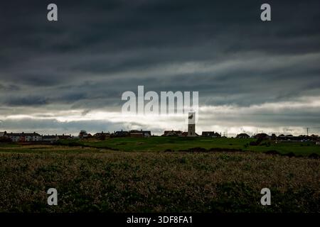Der Chalk Tower des alten Leuchtturms in Flamborough überquert Felder mit Häusern an der Skyline unter einem dramatischen, stimmungsvollen Himmel in East Yorkshire, England. Stockfoto