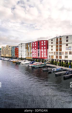 Motorboote vertäuten entlang der Anlegestelle am Nidelva River in Trondheim Norwegen. Farbenfrohe Gebäude auf Stelzen (Brygger) und historische Holzlager Stockfoto