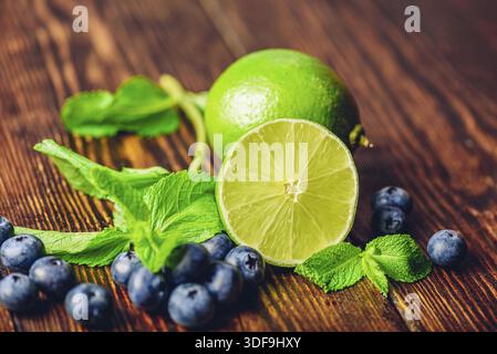 Frische Heidelbeeren, die Hälfte Limetten- und Minzblätter auf Holztisch. Zutaten für die Zubereitung von infundiertem Wasser Stockfoto
