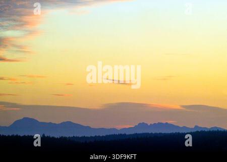 Ein atemberaubendes Landschaftsbild am frühen Morgen mit Blick über das Salish Meer auf die beleuchteten Berge und den farbenfrohen Himmel des Festlandes von British Columbia. Stockfoto
