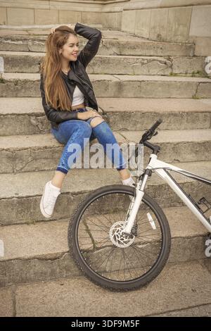 Lächelndes Mädchen mit Fahrrad, das auf Stufen sitzt Stockfoto