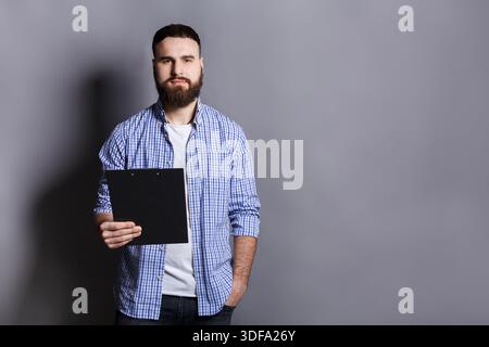 Junger ernsthafter bärtiger Mann, der mit Mappe steht Stockfoto