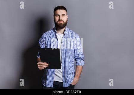 Junger ernsthafter bärtiger Mann, der mit Mappe steht Stockfoto