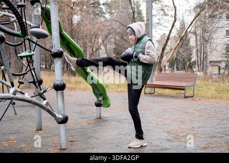 Ein Mann in Trainingsanzug und Hut dehnt sich mit Boxhandschuhen auf einem Outdoor-Sportplatz. Sport bei kaltem Wetter. Stockfoto