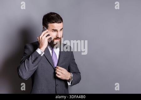 Konzentrierter bärtiger Geschäftsmann, der am Telefon spricht Stockfoto