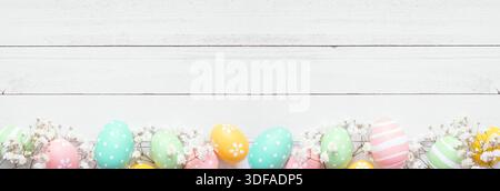 Ostereier in Pastellfarben und weiße Frühlingsblumen. Ansicht von oben nach unten unterer Rand vor einem weißen Holzbanner Hintergrund. Kopierbereich. Stockfoto