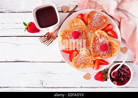Herzförmige Pfannkuchen zum Valentinstag oder Muttertag. Ansicht von oben nach unten auf weißem Holzhintergrund mit Kopierraum. Stockfoto