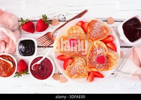 Herzförmige Pfannkuchen zum Valentinstag oder Muttertag. Blick von oben auf weißem Holzhintergrund. Stockfoto