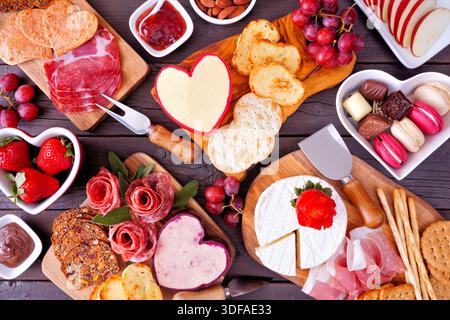 Valentinstag-Motiv mit Wurstwaren-Tischszene vor dunklem Holzhintergrund. Auswahl an Käse, Fleisch, Obst und süßen Vorspeisen. Draufsicht. Stockfoto