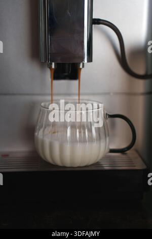 Kaffeemaschine – frisch gebrühter Espresso in eine transparente Tasse Milch auf einer eleganten Küchenarbeitsfläche aus Metall für einen gemütlichen und frischen Morgen Stockfoto