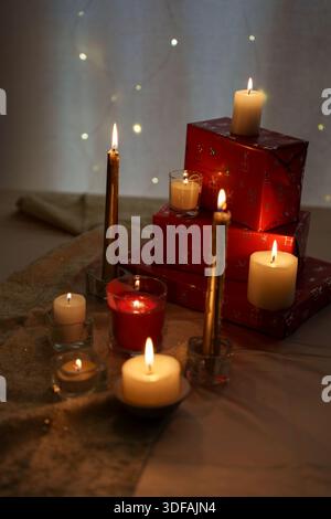 Gemütliches Urlaubsambiente mit leuchtenden Kerzen und gewickelten Geschenken auf weichem Stoffhintergrund, beleuchtet durch warmes Licht und sanfte Feenlichter, die einen schaffen Stockfoto