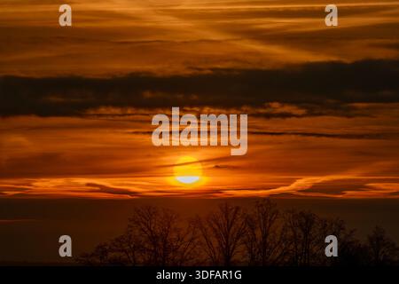 Farbige Sonnenaufgänge mit Wolken und Silhouetten von Bäumen am frostigen Wintermorgen Stockfoto