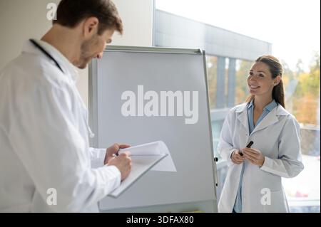 Eine Ärztin, die neben dem Flipchart steht und einem neuen Arzt etwas vorstellt Stockfoto