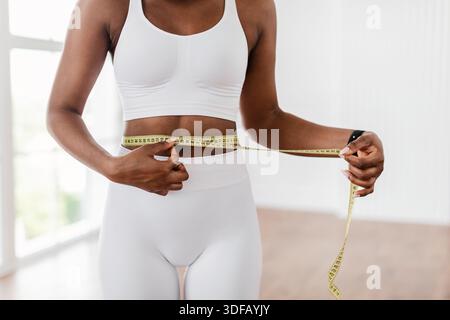 Nahaufnahme einer schwarzen Frau, die die Taille mit Klebeband misst. Schlankheitskonzept Stockfoto