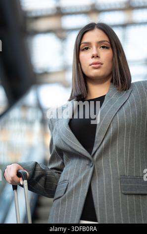 Junge Berufsfrau auf dem Weg zu einer Geschäftsreise, die mit ihrem Gepäckgriff in einem Flughafen oder Bahnhof steht Stockfoto