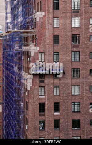 Arbeiter an Gerüsten, die Ziegelfassaden umdeuten, defekte Ziegelsteine und Mörtel entfernen, wie es das New York City Local Law 11 vorschreibt, das Reparaturen, regelmäßige Inspektionen und Wartung von Gebäudefassaden verlangt, Freitag, 31. Oktober 2025. Foto: Jennifer Graylock-Alamy Stockfoto