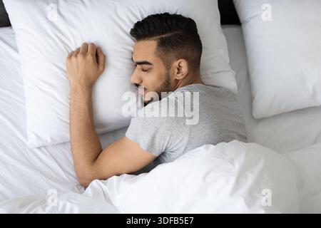 Junger arabischer Mann genießt tiefen Schlaf in einem gemütlichen Schlafzimmer mit weichen Betten und ruhiger Atmosphäre Stockfoto