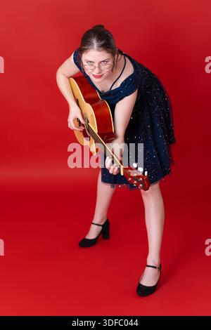 Hochwinkelaufnahme einer Gitarristin, die klassische Gitarre zupft und in die Kamera schaut. Europäische junge Erwachsene Sängerin Songwriterin, Teil von Gen Z, Wear Stockfoto