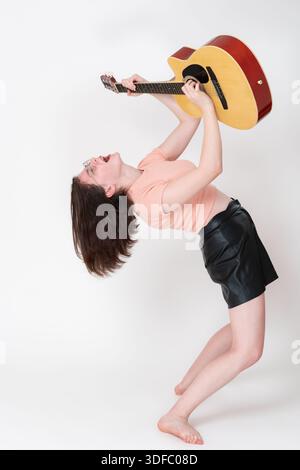 Emotionale Gitarristin spielt Gitarre und schreit Song, beugt sich nach hinten und hebt die Gitarre auf, spielt leidenschaftlich. Barfuß junge fema Stockfoto