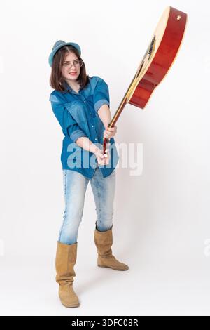 Eine Gitarristin mit negativem Ausdruck auf der gespenstischen Gitarre vor ihr, die frustriert ist, um verhasste akustische musikalische Inst zu zerschlagen und zu brechen Stockfoto