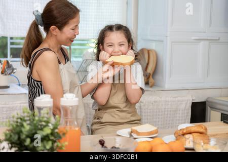 Gemeinsame Aktivitäten während der Feiertage. Eltern und Kinder essen zusammen, Mutter bereitet das Frühstück für die Tochter am Morgen vor, genießen Sie, kleine Stockfoto