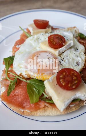 Frisch zubereiteter herzhafter Toast mit Lachs, Spiegeleiern, Brie-Käse, Tomaten und Rucola Stockfoto