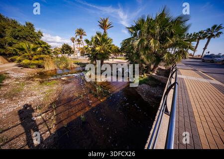 Blick auf den Küstenweg mit kleinen Wasserkanälen, üppigen Palmen und dem Übergang zwischen dem Stadtpark und der Mittelmeerküste Stockfoto