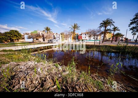 Eine weite Landschaft zeigt die Reflexion farbenfroher mediterraner Häuser in einem kleinen Pool mit Wasser, mit einer Brücke und Palmen unter einem schimmernden Himmel Stockfoto