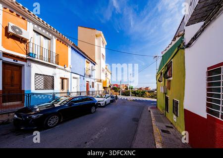 Ein Weitwinkelblick auf die Straße mit grünen, blauen und orangen Häusern, die typisch für Villajoyosa sind, mit modernen Autos, die entlang des Bürgersteigs geparkt werden. Stockfoto