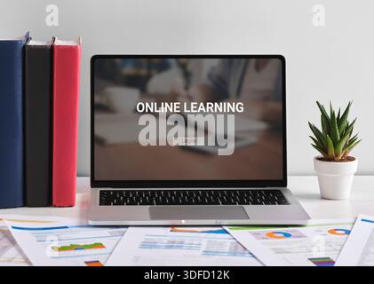 Online-Lernwebsite, die auf einem Laptop-Bildschirm auf einem weißen Schreibtisch mit Dokumenten, Büchern und einer Anlage angezeigt wird und das Konzept der Fernausbildung fördert Stockfoto