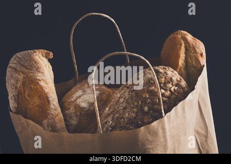 Papiertüte mit Brotsortiment auf schwarzem Hintergrund Stockfoto