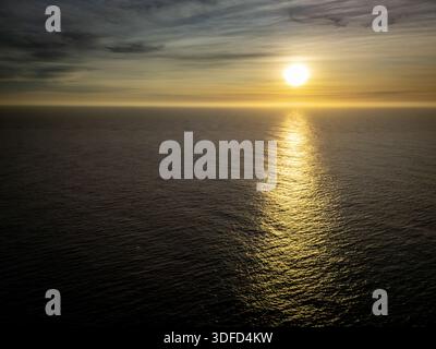 Aus der Vogelperspektive auf die Sonne reflektiert auf dem dunklen Meereswasser und bildet einen glitzernden goldenen Pfad zum Horizont, Kiama, New South Wales, Australien. Stockfoto