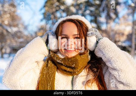Porträt der glücklichen jungen Frau in Kapselgehörschützern und im Winter im warmen Schal im Freien Stockfoto