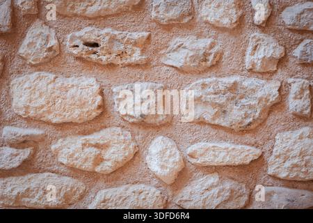 Rustikale Steinmauertextur bildet einen natürlichen architektonischen Hintergrund mit rauen beigen und hellbraunen Felsen und altem Mörtelmuster Stockfoto