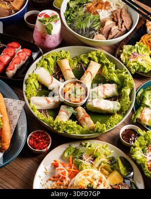 Farbenfrohe vietnamesische Gerichte wie Frühlingsrollen, Salate und Grillfleisch auf einem rustikalen Holztisch, perfekt für kulturelle Projekte oder kulinarische Themen Stockfoto