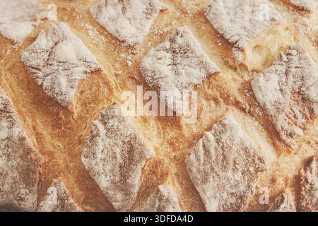 Frisch gebackenes, handwerkliches Brot mit goldener Kruste und Mehlstaub auf rustikaler Oberfläche Stockfoto