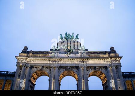 Flacher Blick auf den beleuchteten oberen Teil des Triumphbogens Cinquantenaire mit Bronzestatuen und einem zentralen Wappen, gegenüber dem Stockfoto
