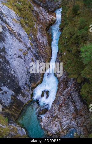 Blick von oben auf einen Wasserfall, der durch eine enge felsige Schlucht in einen türkisfarbenen Tauchpool fließt. Stockfoto