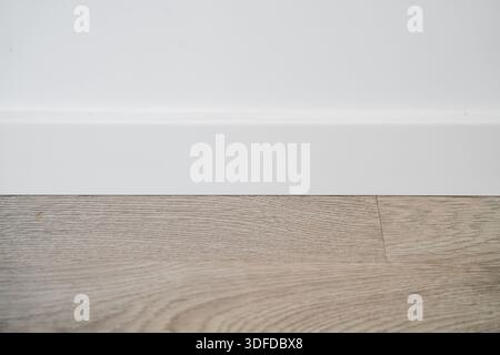 Minimale weiße Innenwand mit Holzboden und Fußplatte, sauberer Hintergrund für leeren Raum mit Kopierraum für Design und Immobilien Stockfoto