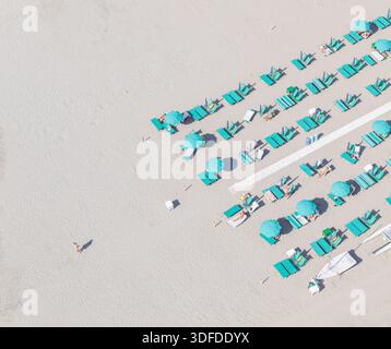 Aus der Vogelperspektive sehen Sie die Reihen von hellen türkisfarbenen Sonnenschirmen und Sonnenliegen im Kontrast zu der weiten Weite des hellen Sandes, Forte dei Marmi, Toskana Stockfoto